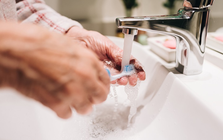 Person washing their toothbrush and hands simultaneously