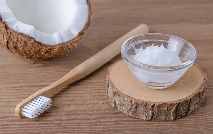 A toothbrush and a coconut and a bowl of shredded coconut from a different coconut
