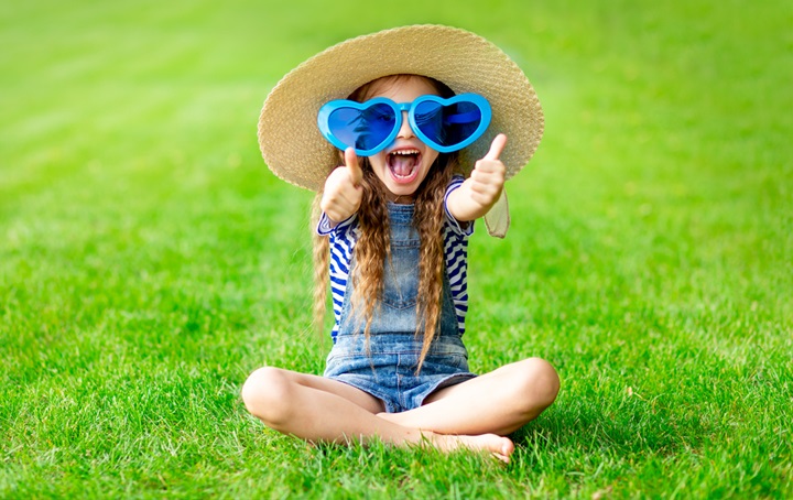 A young girl with shades, smiling while sitting in the grass