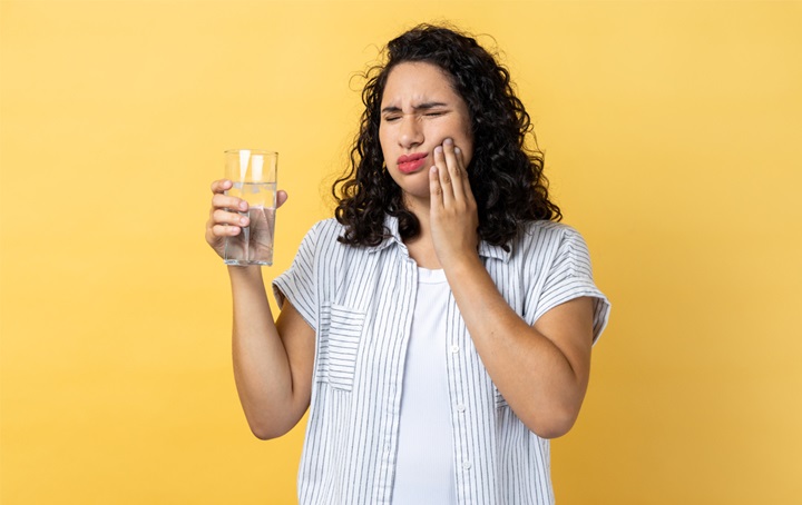 A woman dealing with sensitive teeth when drinking cold water.