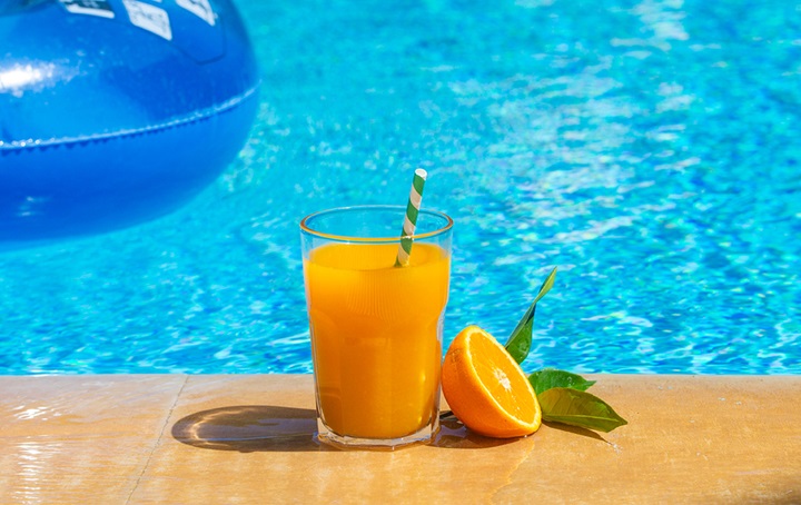 Glass of orange juice next to pool